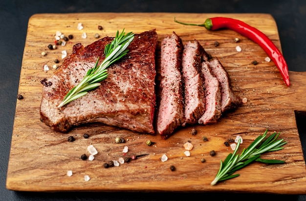 grilled beef steak on a cutting board with spices on a stone background