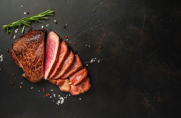 Grilled beef steak, herbs and spices on a stone background, top view