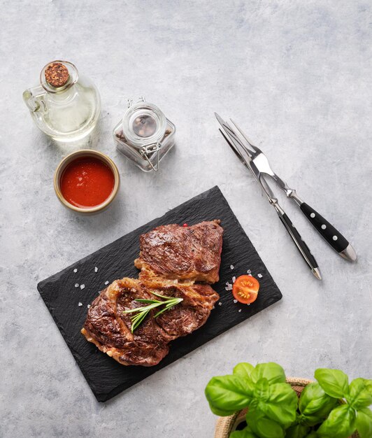 Grilled beef steak with sauce oil and basil on black slate on light background