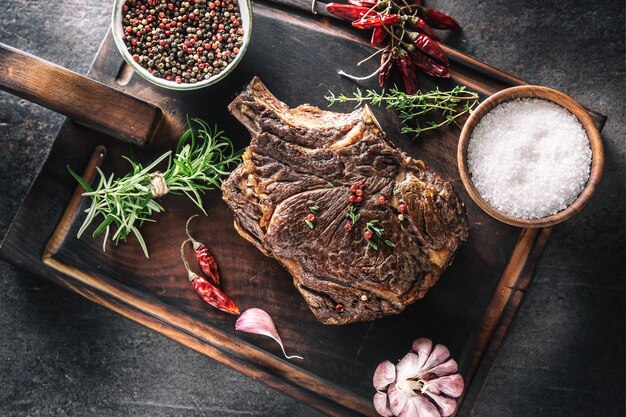 Photo grilled beef steak with spices herbs salt pepper and garlic on wooden cutting board - top of view.