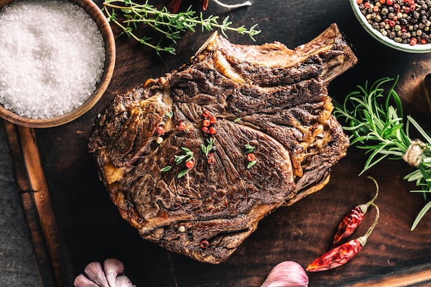 Grilled beef steak with spices herbs salt pepper and garlic on wooden cutting board - Top of view.