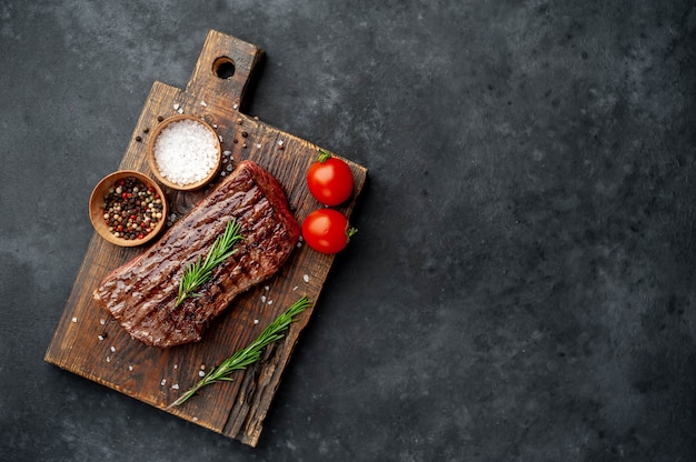 grilled beef steak on a wooden board with spices on a stone background with copy space for your text