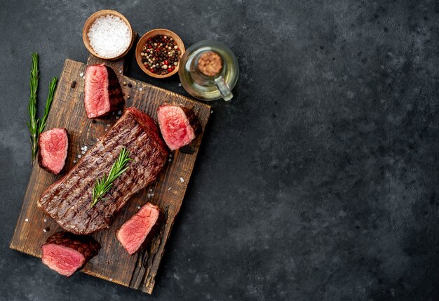 grilled beef steak on a wooden board with spices on a stone background with copy space for your text