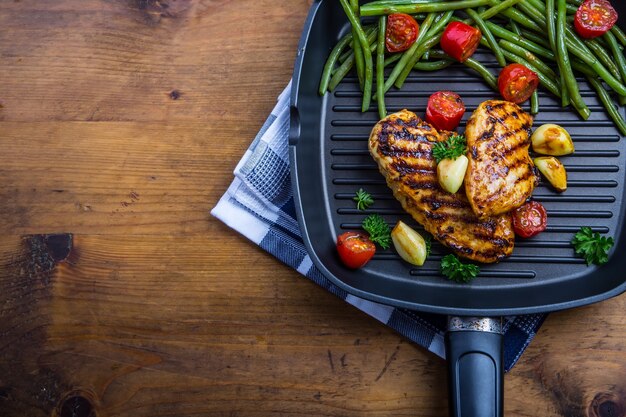 Photo grilled chicken breast in different variations with cherry tomatoes, green french beans, garlic herbs cut lemon on a wooden board or teflon pan