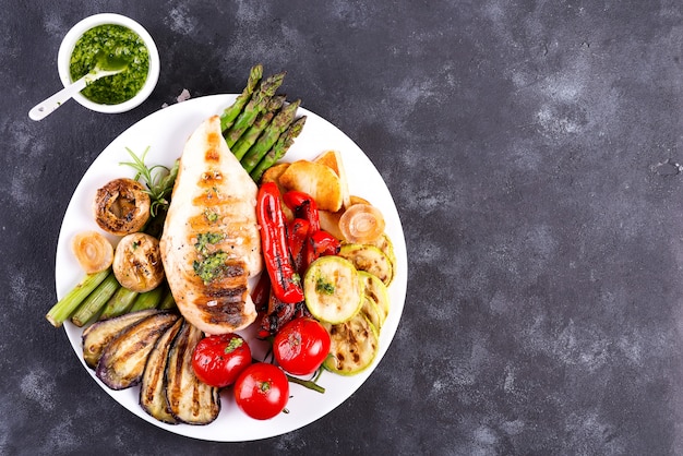 Grilled chicken breast on a plate with tomatoes, asparagus and mushrooms on a stone, flat lay