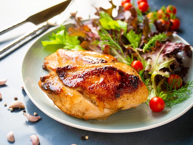 Grilled chicken breast steak serves with fresh cherry tomato and salad on a grey color dish