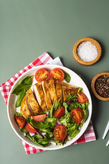 Photo grilled chicken breast with green salad from fresh vegetable salad of lettuce, arugula, spinach, cucumber and tomato on the plate on grey table. healthy lunch menu. diet food backgroind. top view