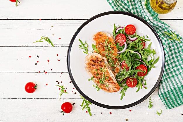 Grilled chicken fillet and fresh vegetable salad of tomatoes,red onion and arugula. Chicken meat salad. Healthy food. Flat lay. Top view.