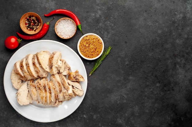 Grilled chicken fillet served in a white plate with spices on a stone background with copy space for your text.