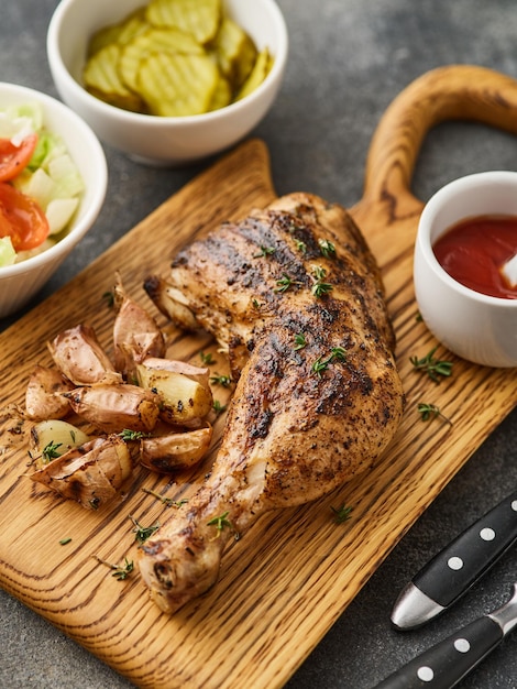 Grilled chicken leg with garlic and pickles on a wooden board