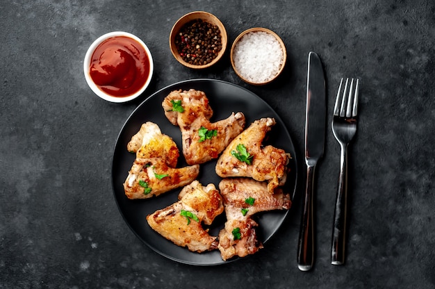 grilled chicken wings in barbecue sauce with parsley on a black plate on a concrete table.