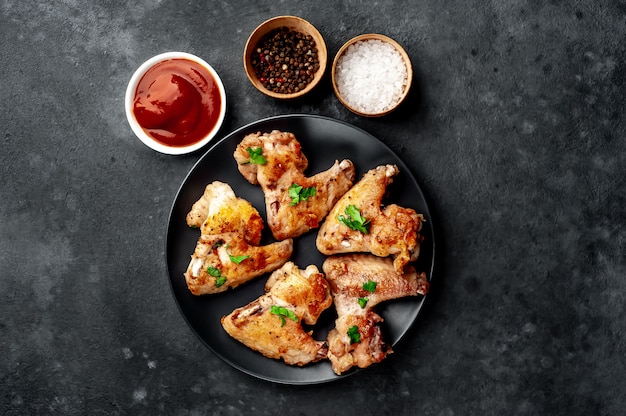 grilled chicken wings in barbecue sauce with parsley on a black plate on a concrete table.