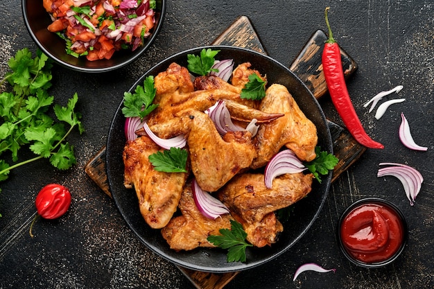 grilled chicken wings or roasted bbq with spices and tomato salsa sauce on a black plate.