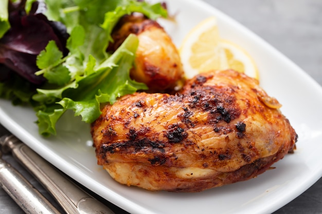 Grilled chicken with lemon and salad on white dish