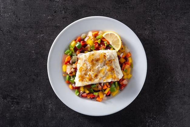 Grilled cod with vegetables in plate on black stone background