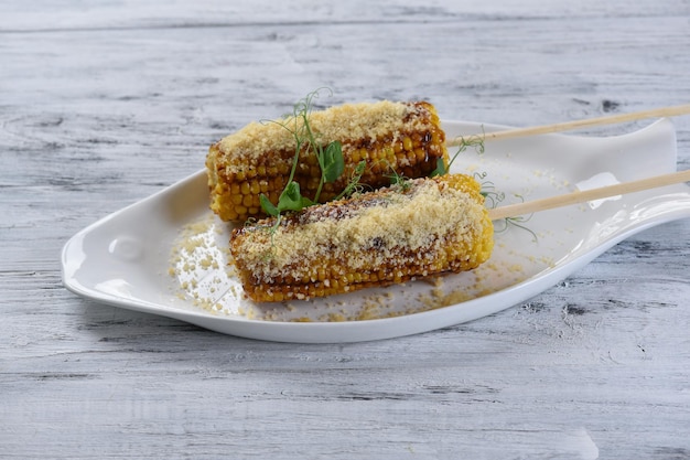 Grilled corn on the cob with parmesan cheese and sprouts, grilled vegetables, top view