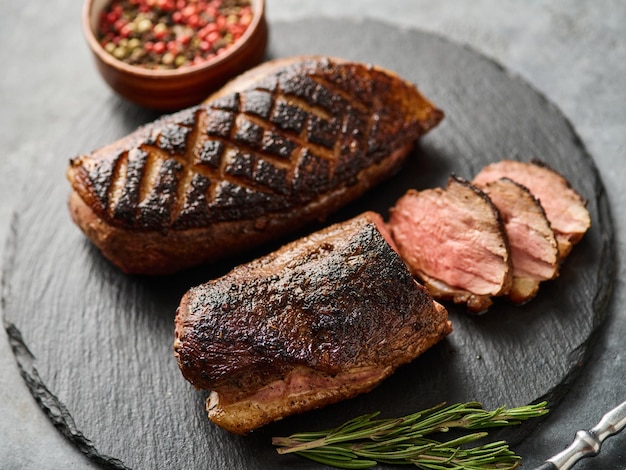 Grilled duck breast on a black slate board with peppers and cherry tomatoes