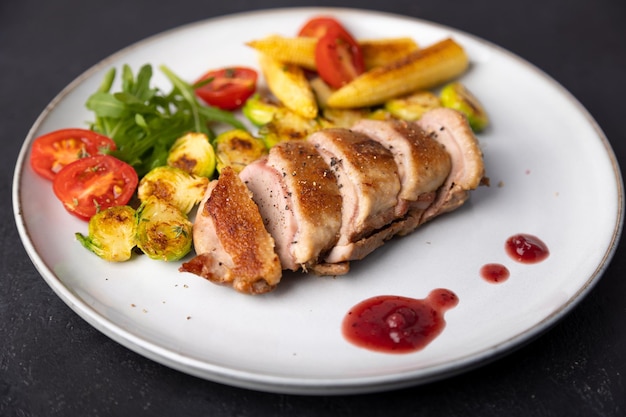 Grilled duck breast fillet with Brussels sprouts mini corn cherry tomatoes arugula and lingonberry sauce Traditional Mediterranean cuisine Selective focus closeup