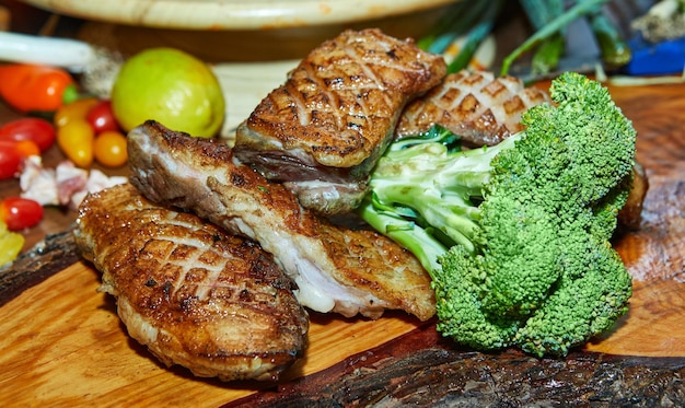 Grilled duck steak with broccoli and vegetables on a wooden board