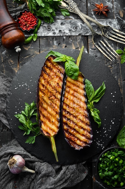 Grilled eggplant with basil on a black stone plate. Top view. Free space for your text.