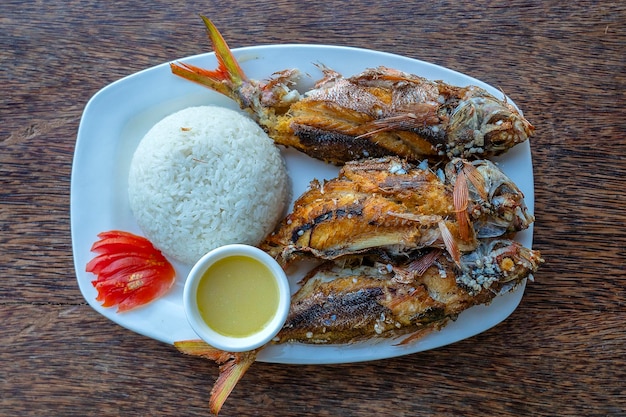 Grilled fish served with sauce rice and tomato close up