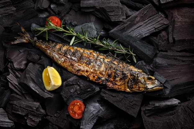 A grilled fish sits on a grill with a lemon and tomatoes.