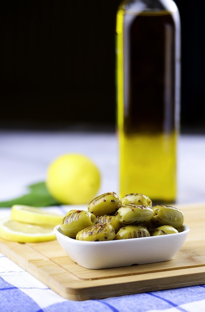 Grilled green olives with rosemary, olive oil and lemon  in a plate on wooden cutting board on table