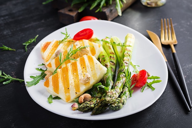 Grilled halloumi cheese salad with tomatoes and asparagus on plate on dark background. Healthy vegetarian food.