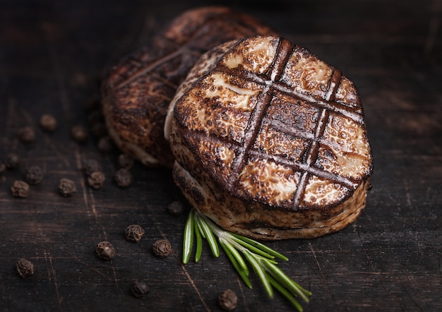 Grilled juicy beef pork steak slice on wooden table with pepper and rosemarine herb