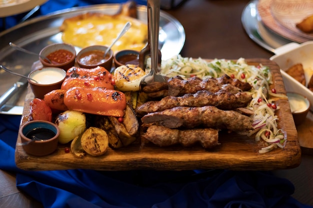 Grilled kebab with spices and grilled vegetables sauces and fresh onions with pomegranate A huge portion for a large company at the restaurant on a wooden rectangular plate