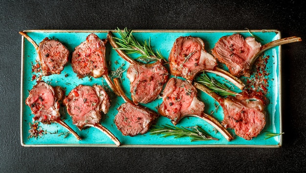 Grilled lamb chops served with rosemary on teal colored platter, top view, horizontal banner