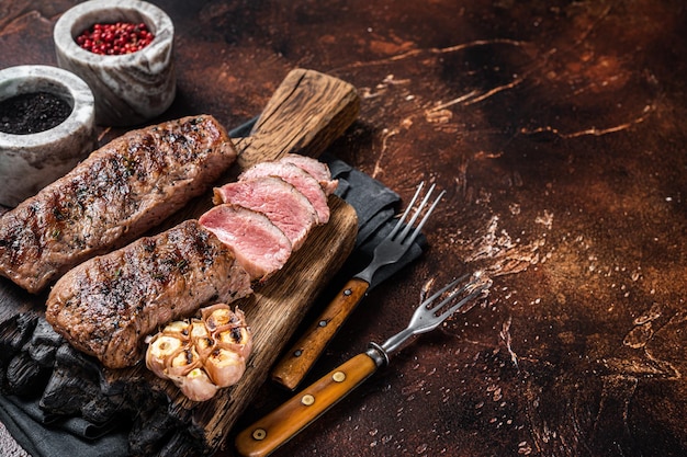 Grilled Lamb sirloin fillet meat on wooden board with herbs mutton loin steak Dark background Top view Copy space