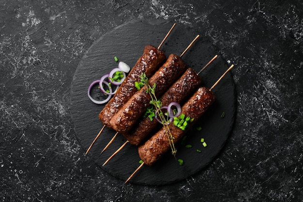 Grilled Lula kebab on skewers with spices in a black plate. On a concrete old table. Top view.