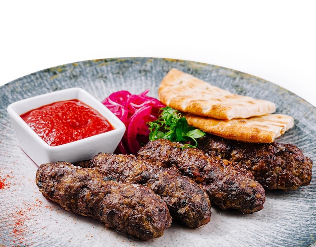 Grilled lula kebab with pita bread adjika and onion on plate isolated on white background