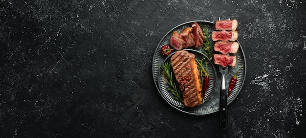 Grilled marbled beef steaks striploin on a fork On a black stone background