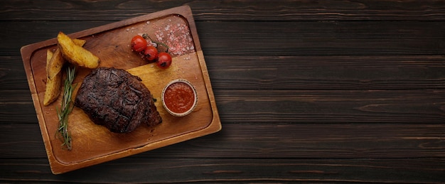 Grilled meat steak with potatoes and tomato sauce on a wooden board