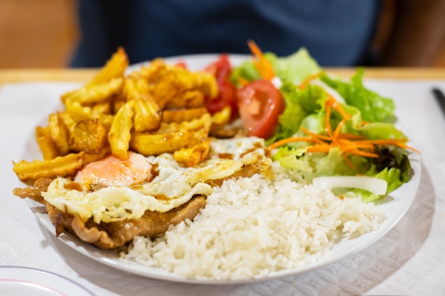 Grilled meat with fried egg rice potato and salad on white plate