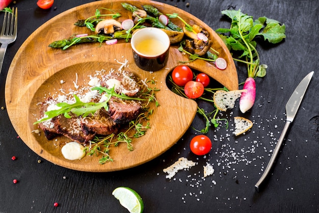 Grilled meat with vegetables in wooden plate on black background