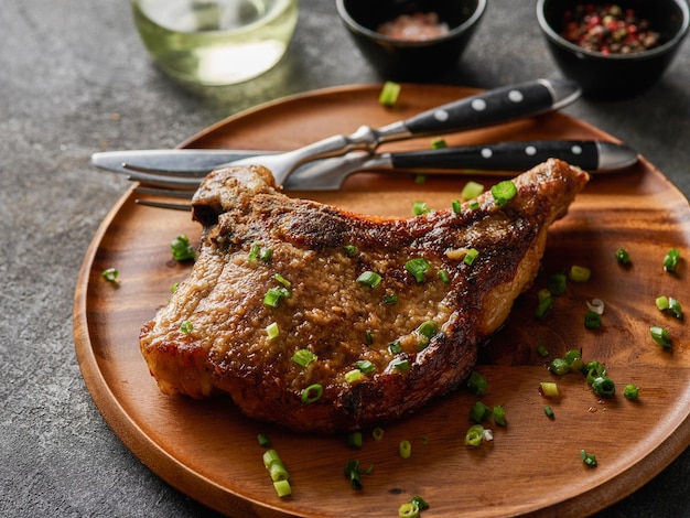 Grilled pork chop on grey plate sprinkled with green onions on the wooden plate grey background