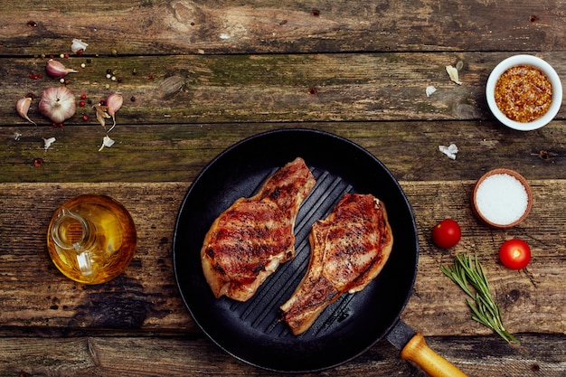 Grilled pork chops in a plate with fork and knife on an old wooden table.