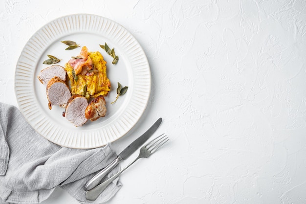 Grilled pork fillet and mash potatoe gratin with sage and prosciutto set, on plate dish, on white stone table, top view flat lay