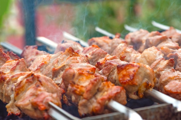 Grilled pork meat on metal skewers. Barbecue cooking. The smoke from the coals develops over the meat. Promotional banner for menu with copy space to insert text.