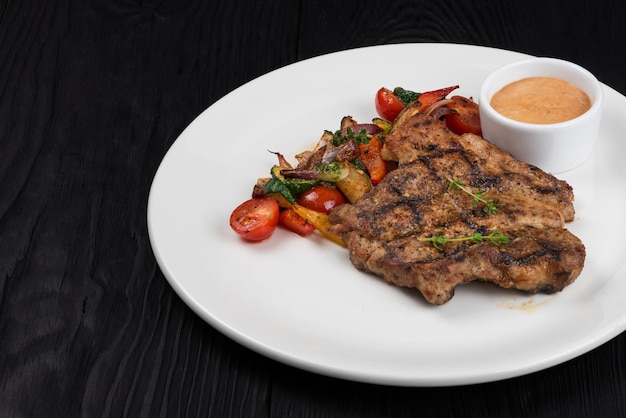 Grilled pork meat steak on white plate on black wooden background