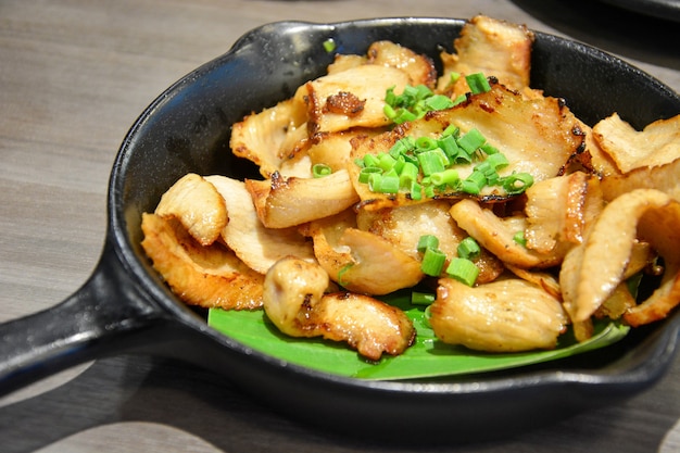 Grilled pork neck with sliced green onions on the top in black pan on wooden table background