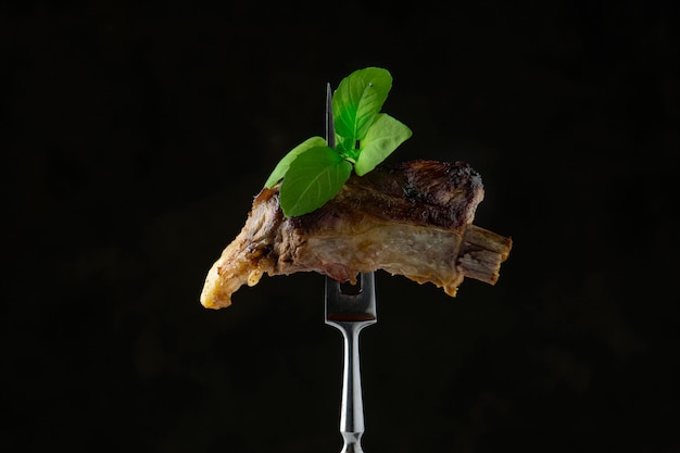 Grilled pork rib with basil leaves on a meat fork