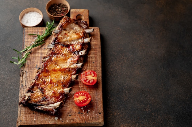 grilled pork ribs on a cutting board with spices on a stone background 