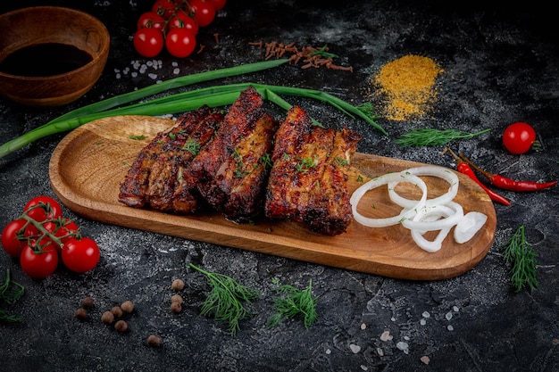 Grilled pork ribs on a dark stone table with vegetables cream and tomato sauce Served on a wooden board Fast food restaurant delivery services