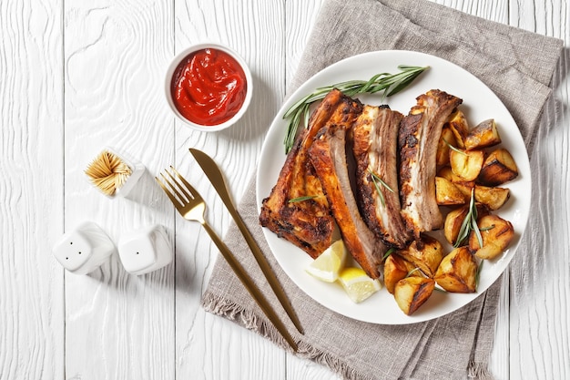 Grilled pork ribs served with roast new potatoes on a white plate on a wooden table horizontal view from above