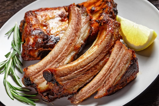 Grilled pork ribs with lemon and rosemary on a plate on a dark wooden table closeup