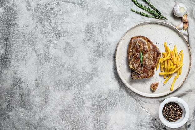 Grilled pork steak on bone with French fries. Gray background. Top view. Space for text